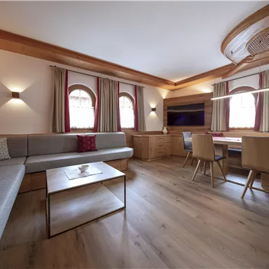 Ein modernes Wohnzimmer mit gemütlicher Sitzecke und Holzdetails. Die großen Fenster lassen viel Licht herein und schaffen eine einladende Atmosphäre.