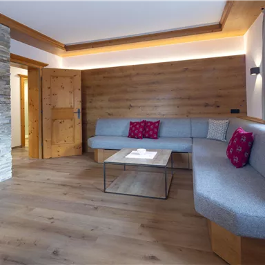 Ein modernes Wohnzimmer mit gemütlicher Sitzecke und Holzverkleidung. Der Raum hat große Fenster und einen Tisch in der Mitte.