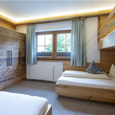 Ein gemütliches Schlafzimmer mit Holzmöbeln und einem Fenster, das viel Licht hereinlässt. Es gibt ein Doppelbett und ein Hochbett, ideal für Familien oder Gruppen.
