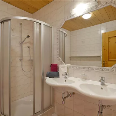 Ein modernes Badezimmer mit einer Dusche und zwei Waschbecken. Die Wände sind gefliest, und es gibt Handtücher in bunten Farben.