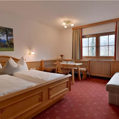 Ein gemütliches Zimmer mit zwei Betten und einem Essbereich. Große Fenster sorgen für viel Tageslicht.