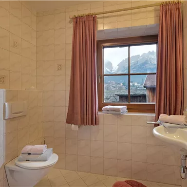 Ein gemütliches Badezimmer mit einem Fenster, das auf die Berge blickt. Die Wände sind hell gefliest und die Vorhänge sind rosa.