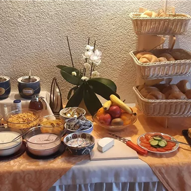 A breakfast buffet with various cereals, yogurt, fresh fruits, and rolls. There are also juices and pastries on a decorated table.