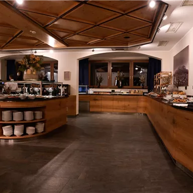 Ein modernes Restaurant mit Holztheke und einem reichhaltigen Buffet. Sanfte Beleuchtung schafft eine einladende Atmosphäre.