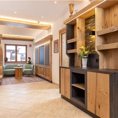 An inviting hallway with modern wooden shelves and bright lighting. On the left side, there is a cozy seating area with plants.