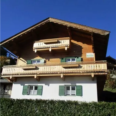 Ein charmantes Holzhaus mit einem Dach aus Ziegeln. Es hat grüne Fensterläden und zwei Balkone.