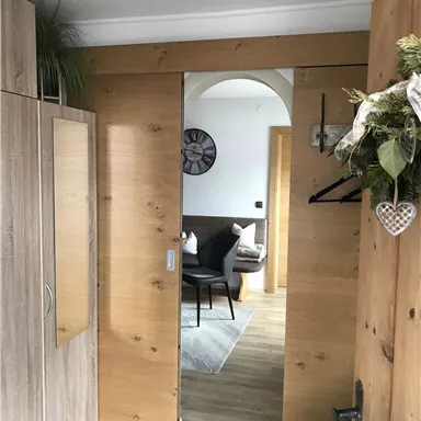 Ein einladender Flur mit einer Holz-Schiebetür. Im Hintergrund sieht man einen gemütlichen Sitzbereich mit einem grauen Teppich und einer Uhr an der Wand.