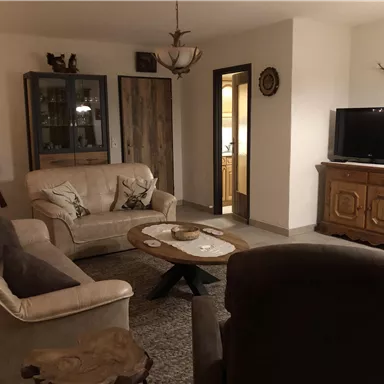A cozy living room with a beige sofa and a brown armchair. There is a coffee table and a television, surrounded by rustic furniture.