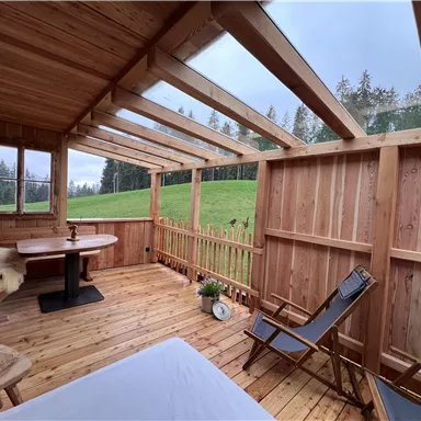A cozy wooden porch overlooking a green meadow. The surroundings are calm and inviting, perfect for relaxing.