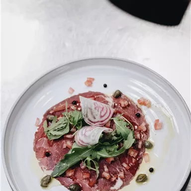 An artistically arranged plate with carpaccio, garnished with arugula, onions, and capers. The colors and textures make the dish appealing and appetizing.