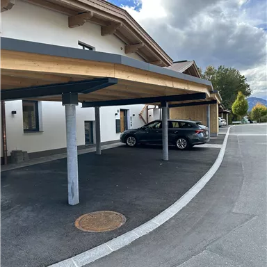 A modern carport in front of a building. In the background, clouds and trees are visible.