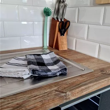 Eine moderne Küchenarbeitsfläche aus Holz mit einem Spülbecken. Es liegen Geschirrtücher und Küchenutensilien auf dem Tisch.