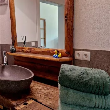 Ein modernes Badezimmer mit einem Holzwaschtisch und einem runden Waschbecken. Auf dem Tisch liegen saftige Handtücher und im Spiegel spiegelt sich eine gemütliche Atmosphäre wider.