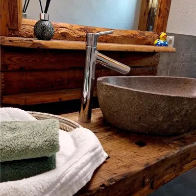 Ein modernes Badezimmer mit einer Holzwaschtisch. Der Waschbecken ist aus Stein und es liegen frische Handtücher bereit.