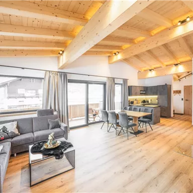 Das Appartement Majestro bietet ein modernes Wohn-Esszimmer mit Holzdecken, großen Fenstern und einen Kaminofen. Es gibt einen Esstisch aus Holz, gemütliche Sitzmöbel und Zugang zu zwei Balkonen. Der große Balkon bietet einen direkten Blick auf den Wilden Kaiser und einen großen Tisch mit Stühlen. Hier können Sie bei einem atemberaubenden Ausblick verweilen. Am zweiten Balkon befindet sich der Whirlpool mit Blick auf die umliegende Bergwelt.
