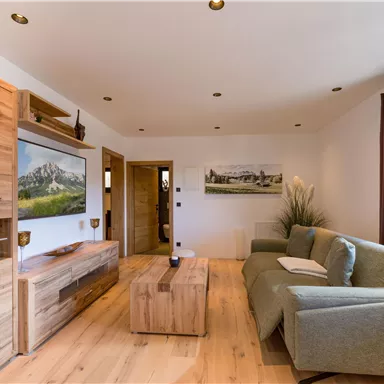 Ein modernes Wohnzimmer mit Holzregalen und einem bequemen Sofa. Die Wände sind hell, und es gibt Kunstwerke sowie angenehmes Licht.