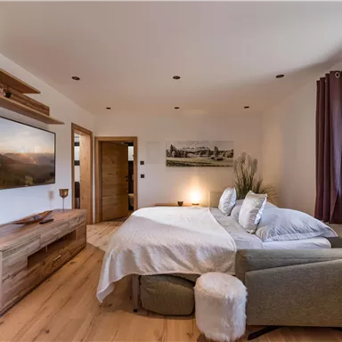 Ein modernes Schlafzimmer mit einem großen Bett und einer gemütlichen Sitzecke. Der Raum hat hölzerne Möbel und wirkt hell und einladend.