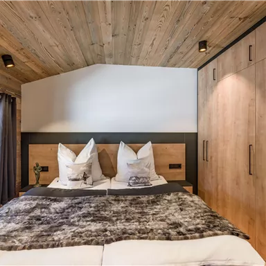 Ein gemütliches Schlafzimmer mit einem großen Bett und Holzpanelen. Die warmen Farben und das moderne Design schaffen eine einladende Atmosphäre.