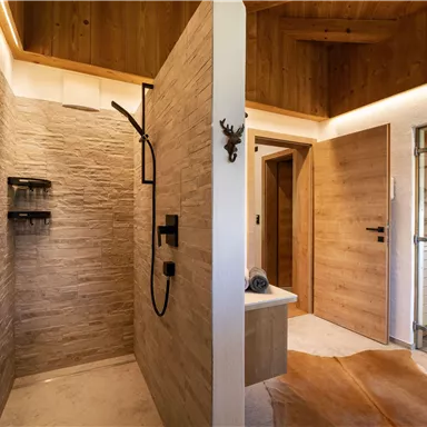 A modern bathroom with a stylish stone shower. On the right, a sauna is visible, surrounded by warm wood tones.