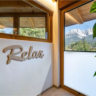 An inviting room with the inscription "Relax" on the wall. Through the windows, one can see an impressive mountain landscape.