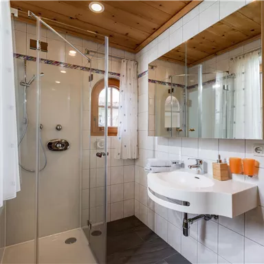 A modern bathroom with a glass shower and an elegant sink. The walls are brightly tiled and there is plenty of natural light.