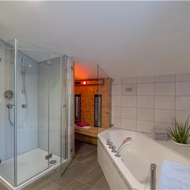 A modern bathroom with a shower cabin and a bathtub. The walls are brightly tiled and the light creates a relaxing atmosphere.