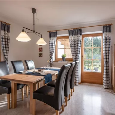 A bright dining room with a wooden table and black chairs. Large windows offer a view of nature outside.