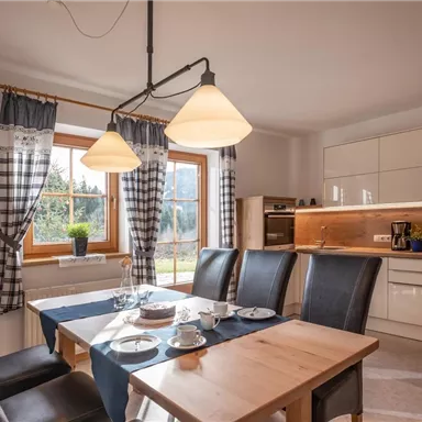 A modern kitchen with a bright dining table and stylish chairs. Large windows provide plenty of daylight and a cozy atmosphere.