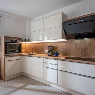 A modern kitchen with white cabinets and wooden details. It includes an oven, a stove, and a coffee machine on the countertop.