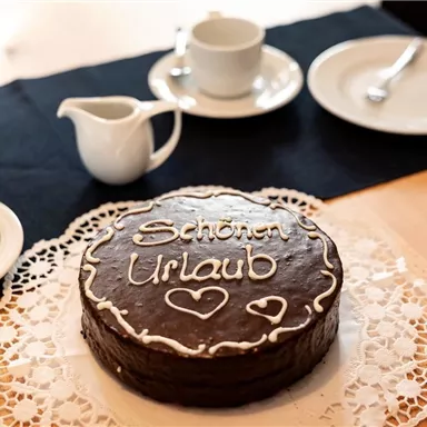 A chocolate cake with the inscription "Happy Holidays" is on a table. Around it are cups and saucers, ready for a coffee round.