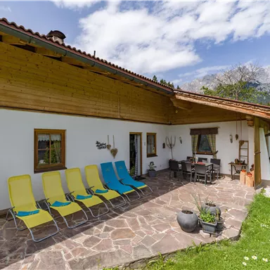 A cozy terrace with loungers and a dining area. In the background, the mountains are visible and the sky is clear.