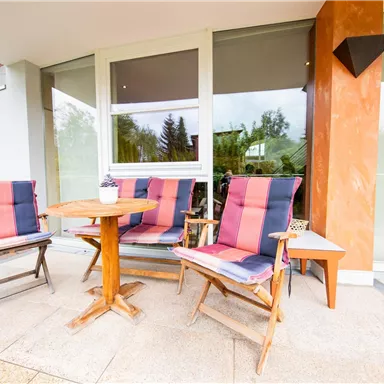 A cozy outdoor area with wooden chairs and a small table. The seating is in bright colors and invites relaxation.