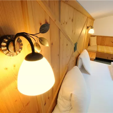 A cozy bedroom with wood paneling and soft lighting. The room features a large bed and a small couch.