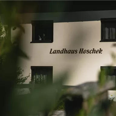 A charming country house with the inscription "Landhaus Hoschek". It is surrounded by plants and radiates an inviting atmosphere.