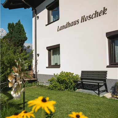 A charming country house named "Landhaus Hoschek" with a beautiful garden. Sunflowers are blooming in the foreground, creating an inviting atmosphere.