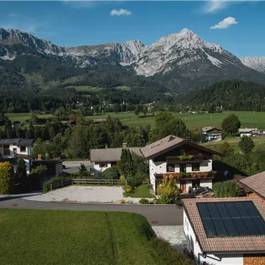 A picturesque landscape with green meadows and charming houses. In the background, impressive mountains rise beneath a clear blue sky.