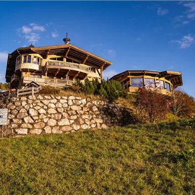 A picturesque mountain cabin on a meadow with beautiful views. The sky is clear and the surroundings are green and inviting.