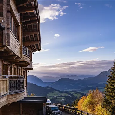 A traditional wooden house with a view of a picturesque mountain landscape. The sky is clear and nature displays autumn colors.