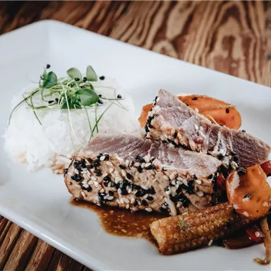 A delicious dish with marinated fish, rice, and colorful vegetables. The presentation is appealingly arranged on a white plate.