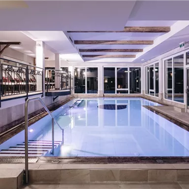 A modern indoor swimming pool with clear water and comfortable seating. Large windows create a bright atmosphere.