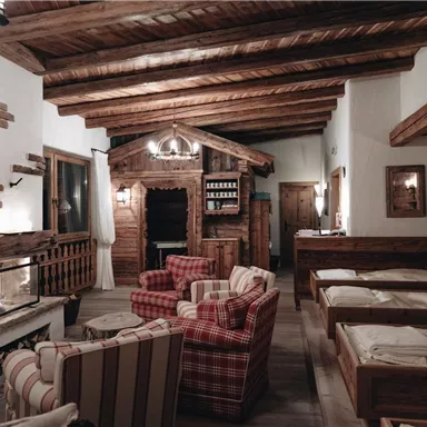 A cozy interior with a beam ceiling, a warm seating area, and an open fireplace. On the right side, there are wooden beds that create an inviting atmosphere.