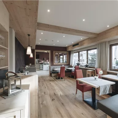 A modern restaurant with wooden decor and large windows. The furnishings are stylish and cozy.