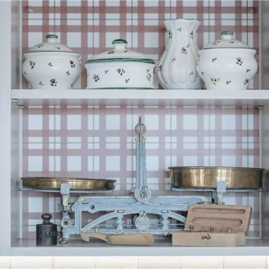 A decorative showcase with various kitchen utensils, including pots and an old scale. The background features a checkered pattern in soft colors.