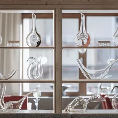 A glass art display case with various decorative glass objects. The objects vary in shape and size and are arranged against a bright background of windows.