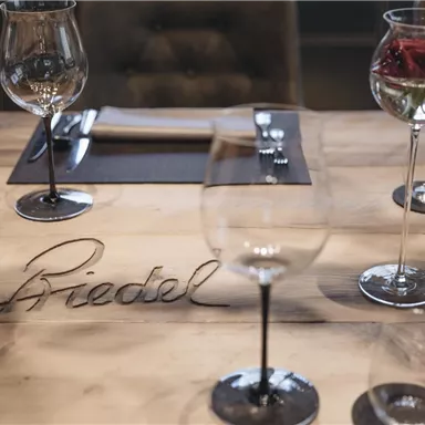 An elegantly set table with wine glasses and a wooden base. On the table is the name "Briedel".