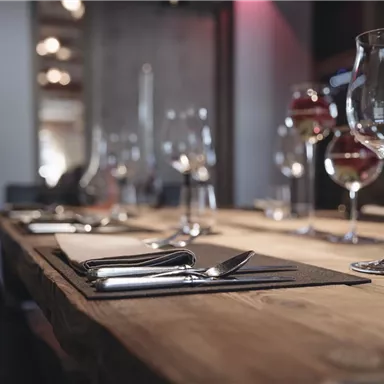 A stylishly set table in an elegant restaurant. Glasses and cutlery are placed on a wooden surface.