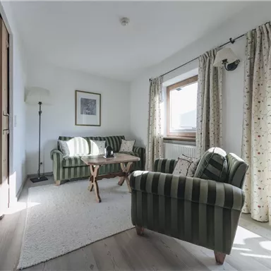 A cozy living room with two striped sofas and a wooden coffee table. Large windows let in plenty of daylight, and the room has an inviting touch.