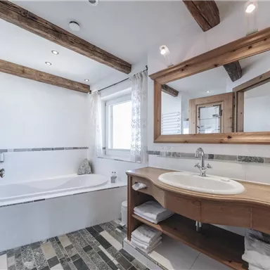 A modern bathroom with a sleek vanity and large mirrors. The wooden beams give the room a cozy atmosphere.