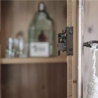 An open wooden cabinet with an old lock. Inside, a few jars and a bottle are visible.