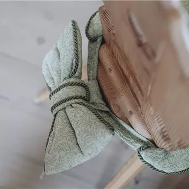 A chair with a mint green cushion tied with a bow. The wooden chair has a natural, warm appearance.